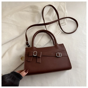 Détail d'un sac à main marron foncé avec nœud décoratif et bandoulière amovible