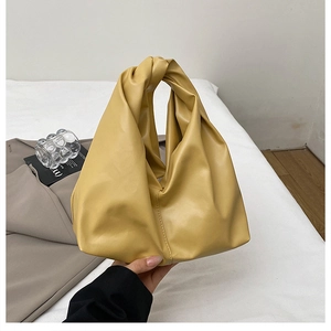 Detailed close-up of a mustard yellow pleated handbag with a knotted handle design