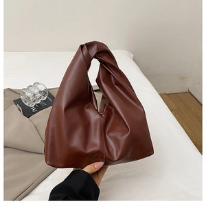 Close-up of brown ruched handbag featuring a minimalist knotted handle and soft leather texture