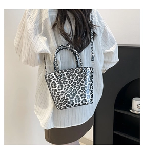 Detail view of the glossy black and white leopard print tote bag worn by a model