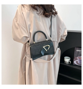Detailed view of black crossbody bag with golden D-shaped buckle and leather trim