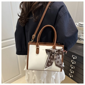 Detail of fashion tote bag with snake skin pattern, brown straps and decorative heart bow