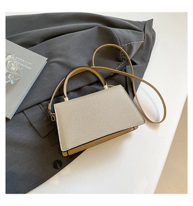 Detailaufnahme einer gelben Lederhandtasche mit beigem Webmuster auf grauem Blazer