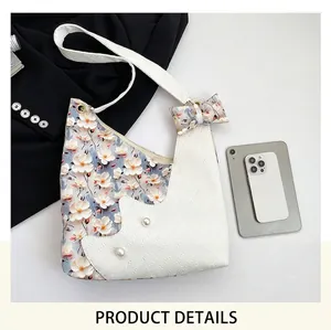 Detail of floral tote bag with bow, pearl accents and crossbody strap on white background