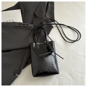 Détail du sac cabas noir brillant minimaliste avec gaufrage mode et poignée décorée de nœuds