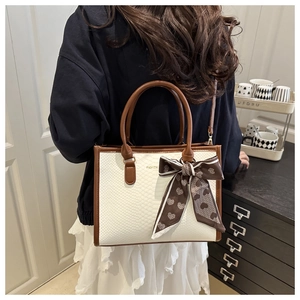 Detail of white snakeskin crossbody bag with brown trim and silk heart bow accessory