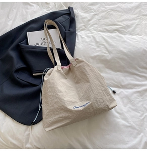 Grand sac cabas beige en nylon avec cordon bleu et broderie sur une literie blanche