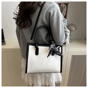 Detail of white snakeskin tote bag with black trim, silk scarf handle and logo text