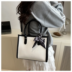 Close-up of white snakeskin texture tote bag with black trim and elegant ribbon bow detail