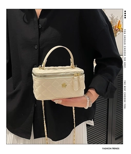 Detail of cream quilted mini box bag with gold floral logo and elegant chain strap