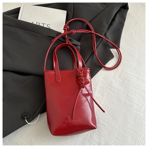 Détail d'un sac à bandoulière en cuir rouge brillant avec poignée et nœuds