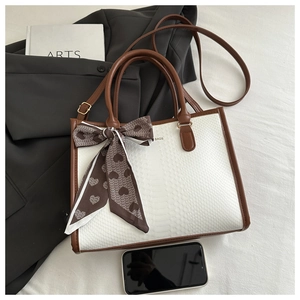 Detail of white snakeskin texture tote bag with brown trim and decorative silk scarf