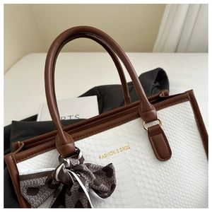 Detail of white snakeskin texture handbag with brown handles and decorative silk bow