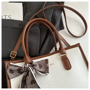 Close-up of cream textured handbag featuring brown leather trim and heart print silk scarf