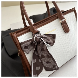 Detail of white snakeskin texture tote bag with brown leather handles and silk bow ribbon