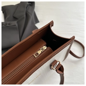 Detailed close-up of white and brown shoulder bag with metal zipper and fine leather texture