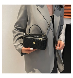 Detail of black quilted chain bag featuring a gold camellia ornament and double zipper
