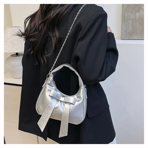 Detail of silver metallic hobo bag featuring large bow and sleek chain strap on a model