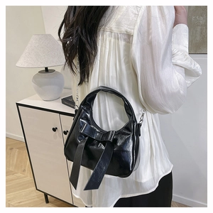 Close-up of black glossy hobo bag featuring a large decorative bow and metallic chain