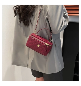 Detail of burgundy quilted crossbody bag with golden flower buckle on a grey blazer