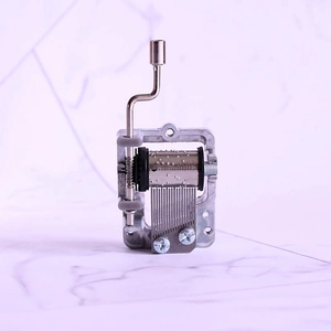 Mechanical hand crank music box movement with silver metal gears on marble surface