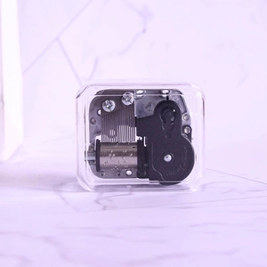 Transparent square music box with mechanical silver clockwork movement on marble background