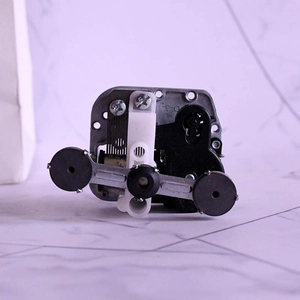 Mechanical wind-up music box movement with gear assembly on white marble surface