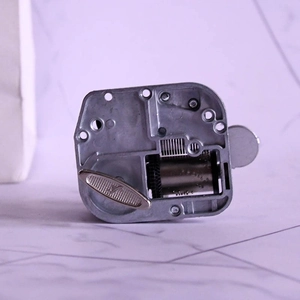 Mechanical wind-up music box movement with silver metal gear set on marble surface