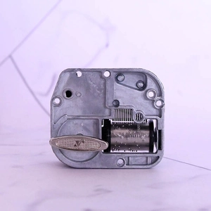 Mechanical wind-up music box movement with silver metal components and winding key