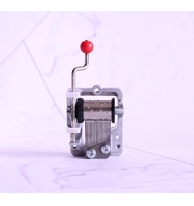 Mini hand-crank music box movement made of zinc alloy with a red bead handle detail