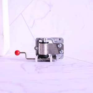 Close-up of a silver mechanical hand-crank music box movement with a red handle