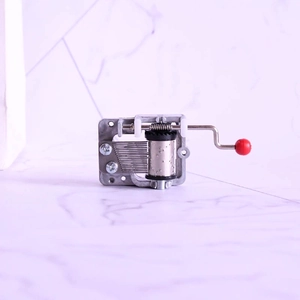 Mechanical hand-crank music box movement with silver metal gears and a red knob