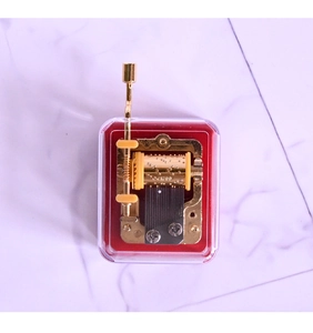 Detailed view of golden mechanical music box movement inside a clear protective case