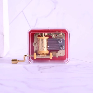 Transparent hand-crank music box with gold metal mechanism and red velvet base