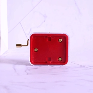 Manual hand-crank music box with a transparent shell and red base with golden crank