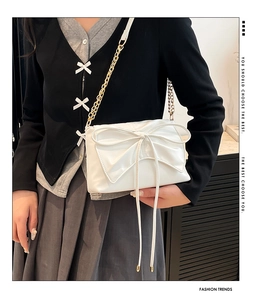 Detail of white PU leather crossbody bag featuring a large bow and gold chain strap