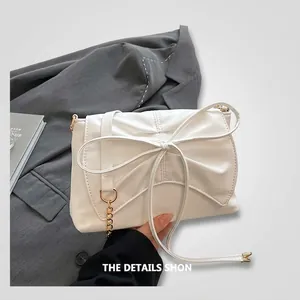 Detail of white faux leather bag with large bow design and gold chain accent