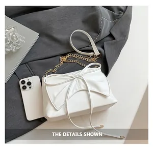 Close-up of white bow shoulder bag with gold chain strap on grey blazer background