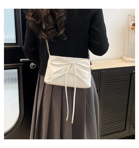 Detail view of a white crossbody bag featuring a large bow and elegant gold chain strap