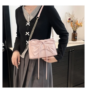 Close-up of pink bow detail and gold chain strap on an elegant ballet-style crossbody bag