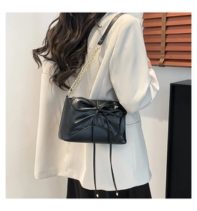 Detail of a chic black shoulder bag featuring a large bow and golden metal chain strap