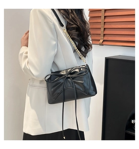 Detail of black bow-knot shoulder bag with polished gold chain strap and glossy leather