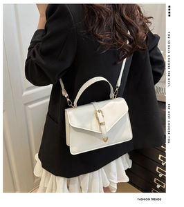 Detail view of white leather crossbody bag with gold buckle and top handle worn by a model
