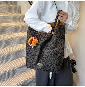 Dettaglio della borsa tote in tela leopardata con targhetta in metallo e ciondolo