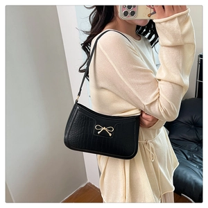 Detail of black crocodile texture baguette bag featuring a gold metal bow on the side