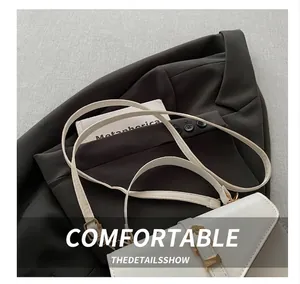 Detail of white PU leather crossbody bag with gold buckle on grey blazer jacket