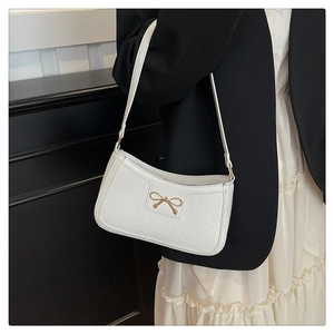 Detail of white croc-effect shoulder bag with golden bow ornament on a female model