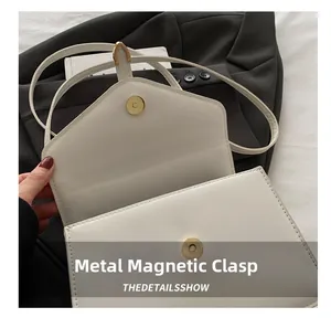 Detailed macro view of the metal magnetic clasp and texture on a white leather bag