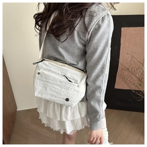 Detailed side view of a white ruched crossbody bag on a model showing modern casual style