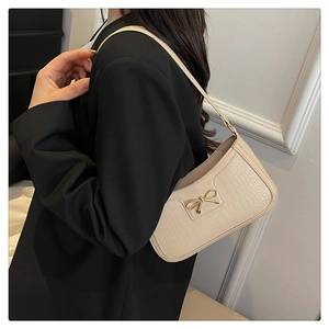 Detail of crocodile pattern texture and golden bow clasp on a beige shoulder bag